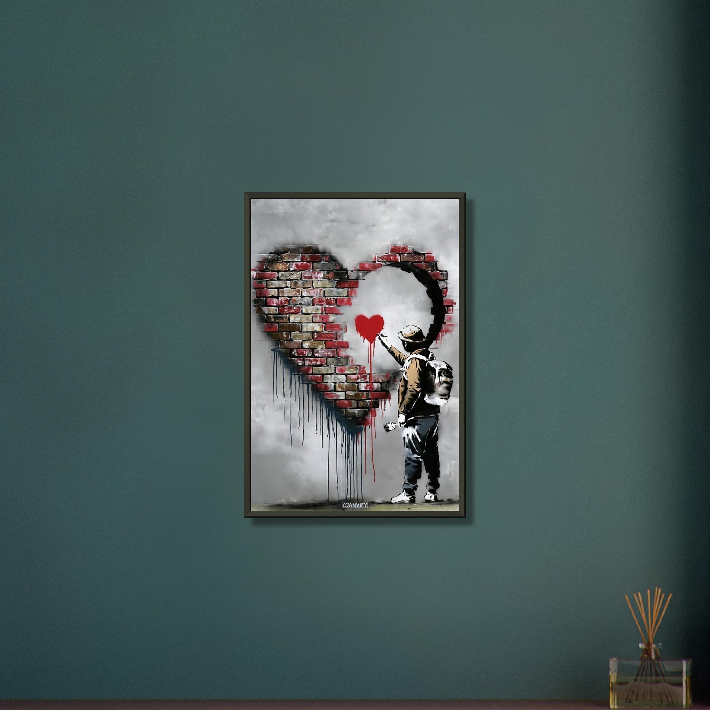 Künstler malt ein kleines rotes Herz in einem großen Herz aus Ziegelsteinen im Banksy Stil auf einem Poster im Metallrahmen