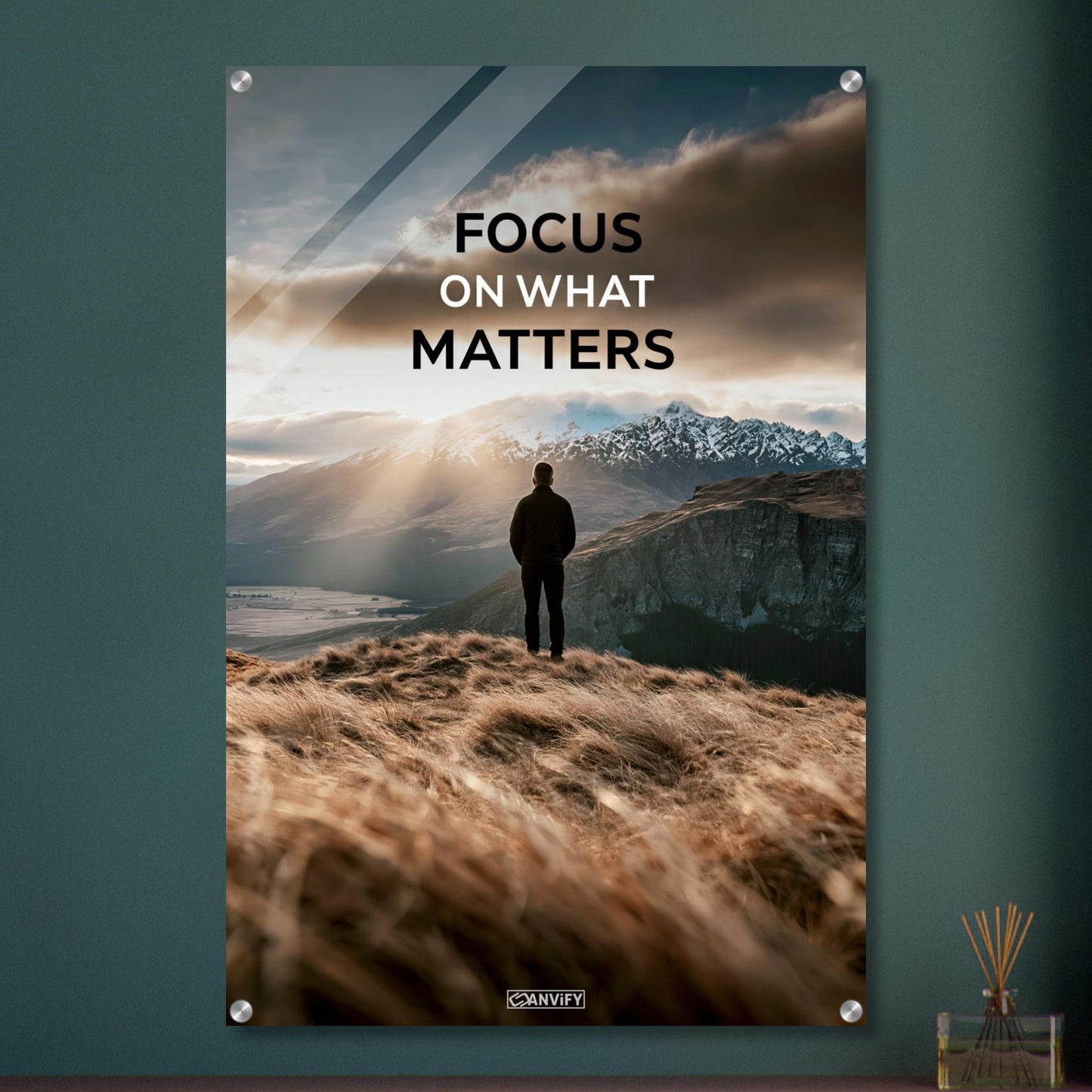 Mann steht auf der Klippe mit dem Rücken zur Kamera und blickt auf den Sonnenaufgang mit dem Motivationsspruch "Focus On What Matters" auf einem Acrylbild