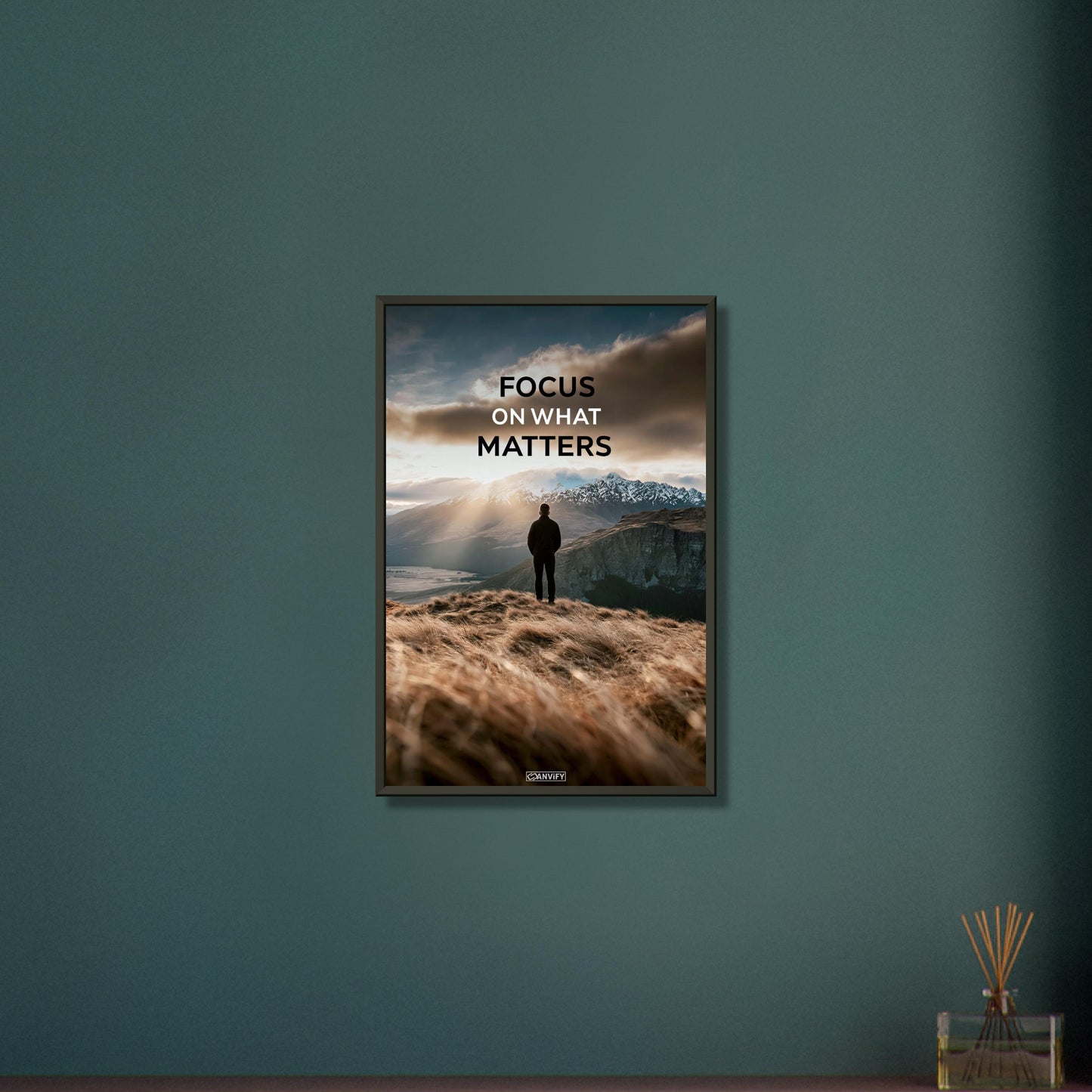 Mann steht auf der Klippe mit dem Rücken zur Kamera und blickt auf den Sonnenaufgang mit dem Motivationsspruch "Focus On What Matters" auf einem Poster im Metallrahmen