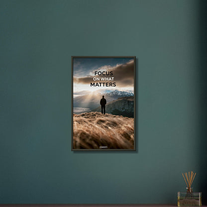 Mann steht auf der Klippe mit dem Rücken zur Kamera und blickt auf den Sonnenaufgang mit dem Motivationsspruch "Focus On What Matters" auf einem Poster im Metallrahmen