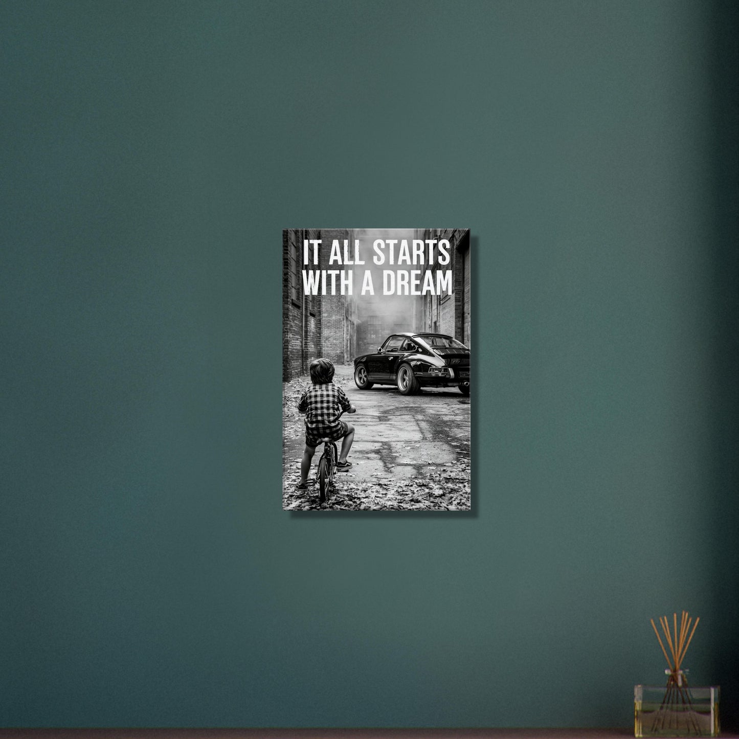 Kleiner Junge auf dem Fahrrad blickt auf einen Porsche 911 mit dem Motivationsspruch "It All Starts With A Dream" auf einer Leinwand