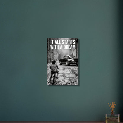 Kleiner Junge auf dem Fahrrad blickt auf einen Porsche 911 mit dem Motivationsspruch "It All Starts With A Dream" auf einer Leinwand