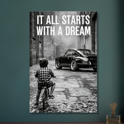 Kleiner Junge auf dem Fahrrad blickt auf einen Porsche 911 mit dem Motivationsspruch "It All Starts With A Dream" auf einer Leinwand