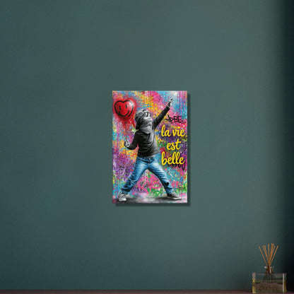 Kleiner Junge mit Basecap, Bandana und einem Herzluftballon in der Hand und einem Spruch "La Vie Est Belle" im Pop Art Stil auf einer Leinwand