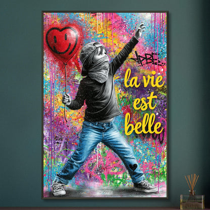 Kleiner Junge mit Basecap, Bandana und einem Herzluftballon in der Hand und einem Spruch "La Vie Est Belle" im Pop Art Stil auf einem Poster im Metallrahmen