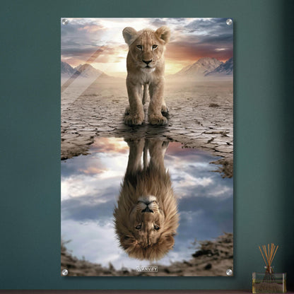 Kleiner Löwe steht vor einer Wasserpfütze, in der sich ein großer Löwe mit Mähne spiegelt – vor Bergpanorama und Sonnenuntergang auf einem Acrylbild