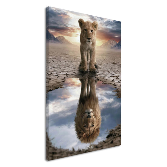 Kleiner Löwe steht vor einer Wasserpfütze, in der sich ein großer Löwe mit Mähne spiegelt – vor Bergpanorama und Sonnenuntergang auf einer Leinwand