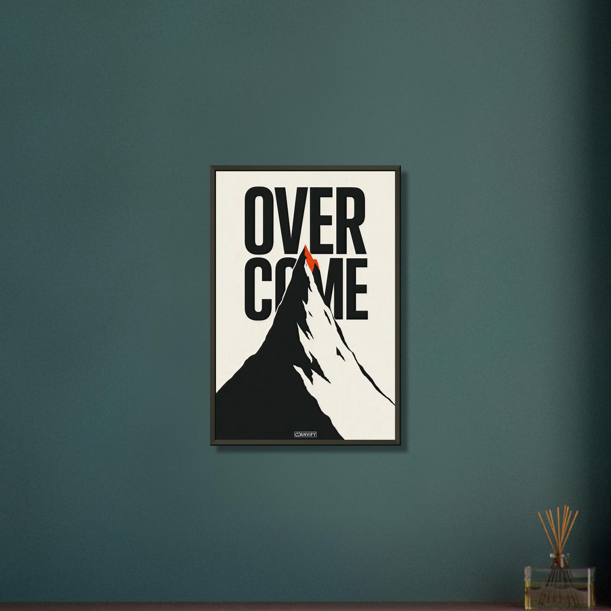 Minimalistisch gezeichneter Berg in Schwarz und Weiß mit einem Spruch 'Overcome' und mit einer roten Bergspitze auf einem Poster im Metallrahmen